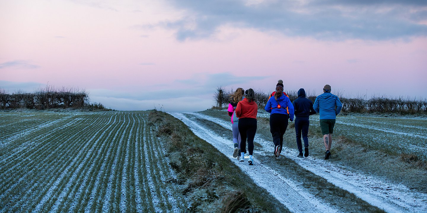 Foto: Eine Gruppe Menschen von hinten zu sehen, die auf einem Feld mit Raureif joggt.