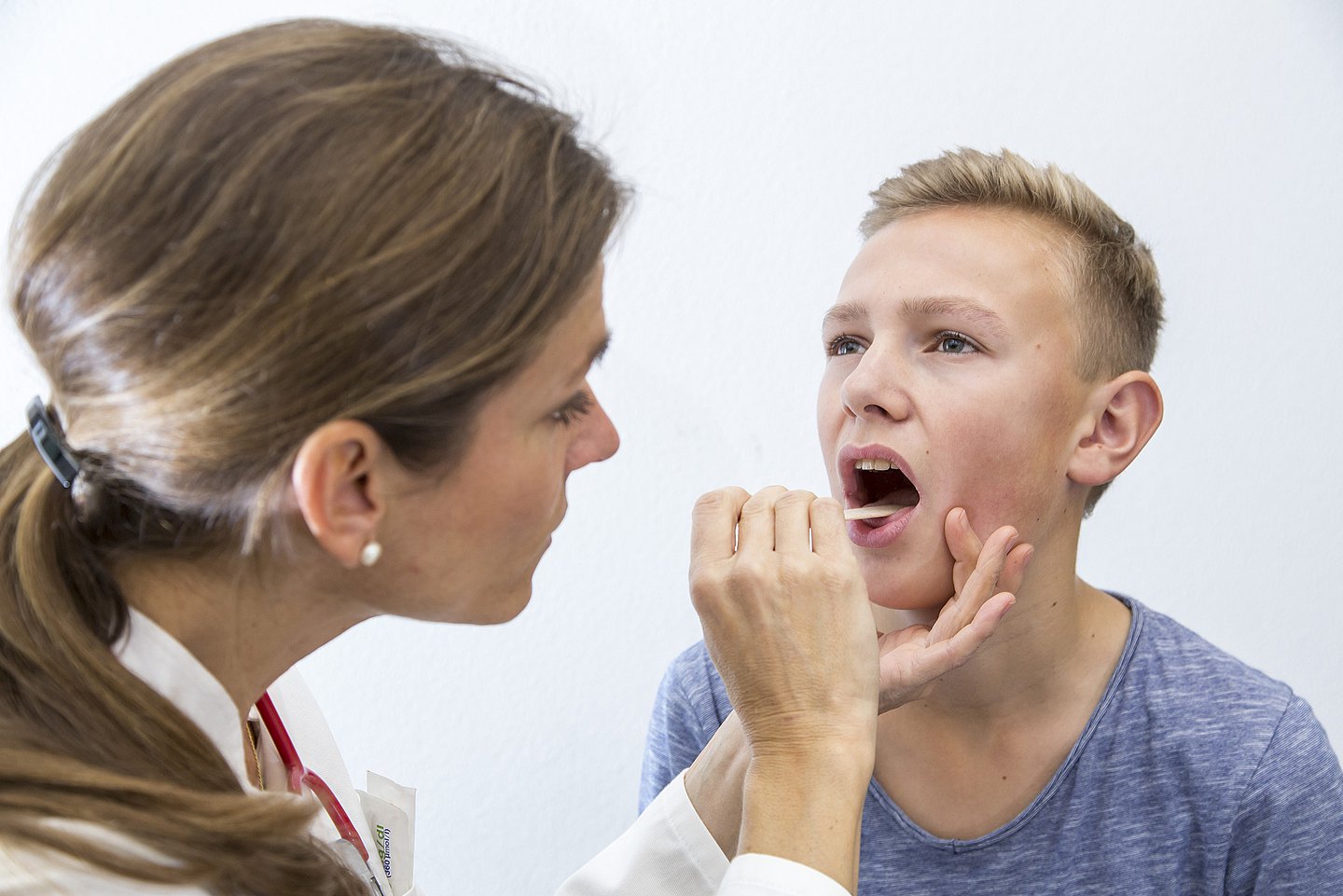 Foto: Eine Ärztin untersucht den Rachen eines Jungen mit einem Stäbchen.