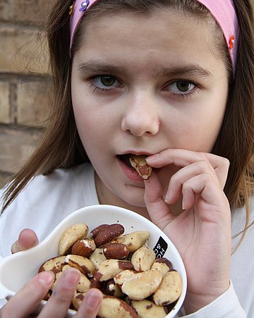 Zink Ein Mädchen nascht Nüsse, weil sie viel Zink und Selen enthalten.