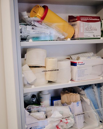 Ein Wandschrank gefüllt mit Arztmaterialien, wie Verbänden, Mundstäbchen, Spritzen und Kochsalzlösung.
