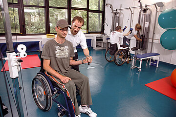 Foto: Patienten in Rollst&uuml;hlen trainieren in einem Trainingszentrum. Im Vordergrund unterst&uuml;tzt ein Physiotherapeut bei einer &Uuml;bung.