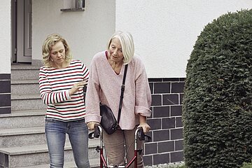 Eine junge Frau st&uuml;tzt eine &auml;ltere Frau mit einem Rollator