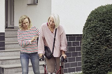 Eine junge Frau stützt eine ältere Frau mit einem Rollator