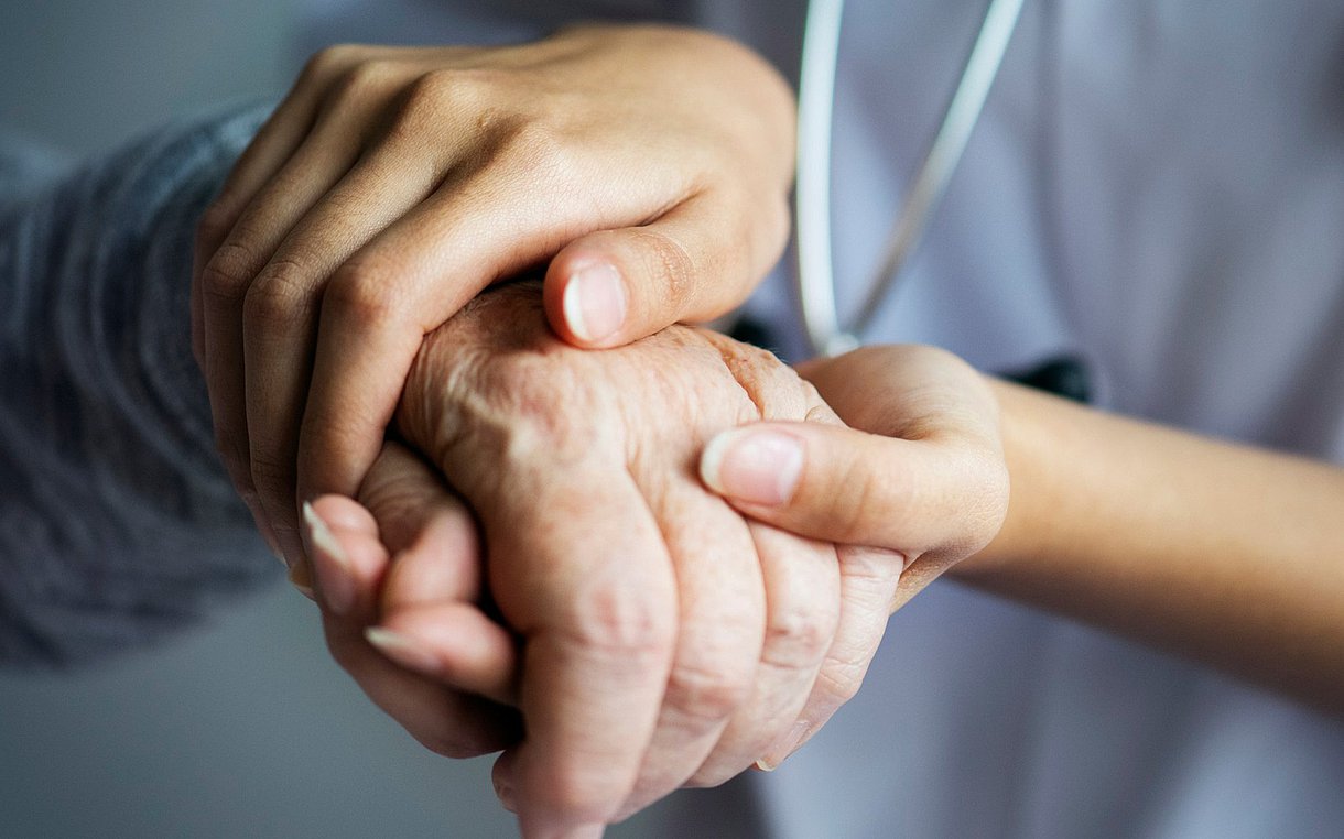 Hände einer jungen Person halten die Hand einer älteren Person.