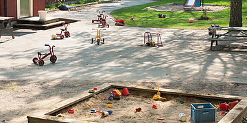 Auf einem Spielplatz mit Sandkiste und Rutsche stehen viele Spielsachen f&uuml;r Kinder, Sandbaufiguren und Roller oder Sitzfahrr&auml;der. Doch es spielen keine Kinder auf dem Spielplatz.