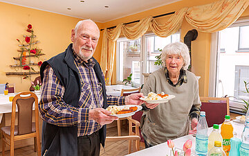 Foto: Ein Ehepaar, das auf einem Pflegebauernhof lebt, h&auml;lt jeweils einen Teller mit Essen in der Hand.