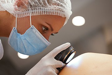 Krebsvorsorge Westfalen-Lippe Foto: Eine Ärztin untersucht die Haut eines Patienten mit einer Lupe.