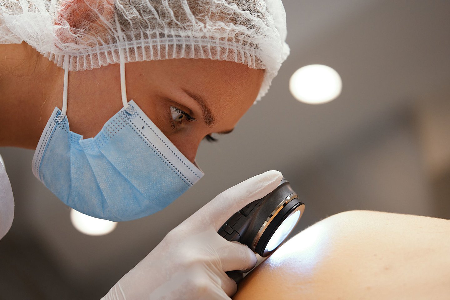 Foto: Eine Ärztin untersucht die Haut eines Patienten mit einer Lupe.