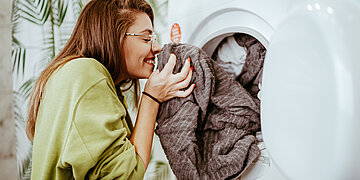Eine Frau riecht an einem Handtuch, das sie frisch aus dem Trockner nimmt.