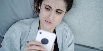 ePa hilft chronisch Kranken Foto einer Frau, die auf einem Sofa liegt und angestrengt in ihr Handy blickt