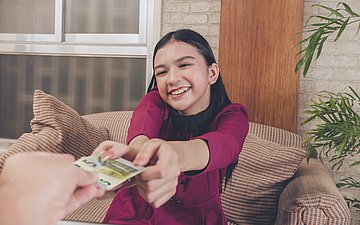 Taschengeld Foto: Ein Mädchen bekommt zwei fünf Euro Scheine gereicht und freut sich.