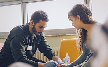 Pfleger Khaled Foto von Pfleger Khaled, der bei Patientin Charlotte einen entzündeten Finger neu verbindet