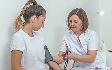 Frauengesundheit Foto einer jungen Frau, bei der eine Ärztin den Blutdruck misst