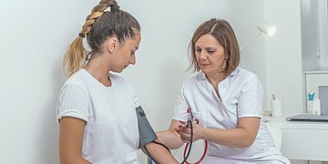 Frauengesundheit Foto einer jungen Frau, bei der eine Ärztin den Blutdruck misst
