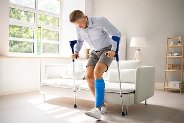 Das Bild zeigt einen Mann mit Kr&uuml;cken, der am linken Bein eine Bandage tr&auml;gt.