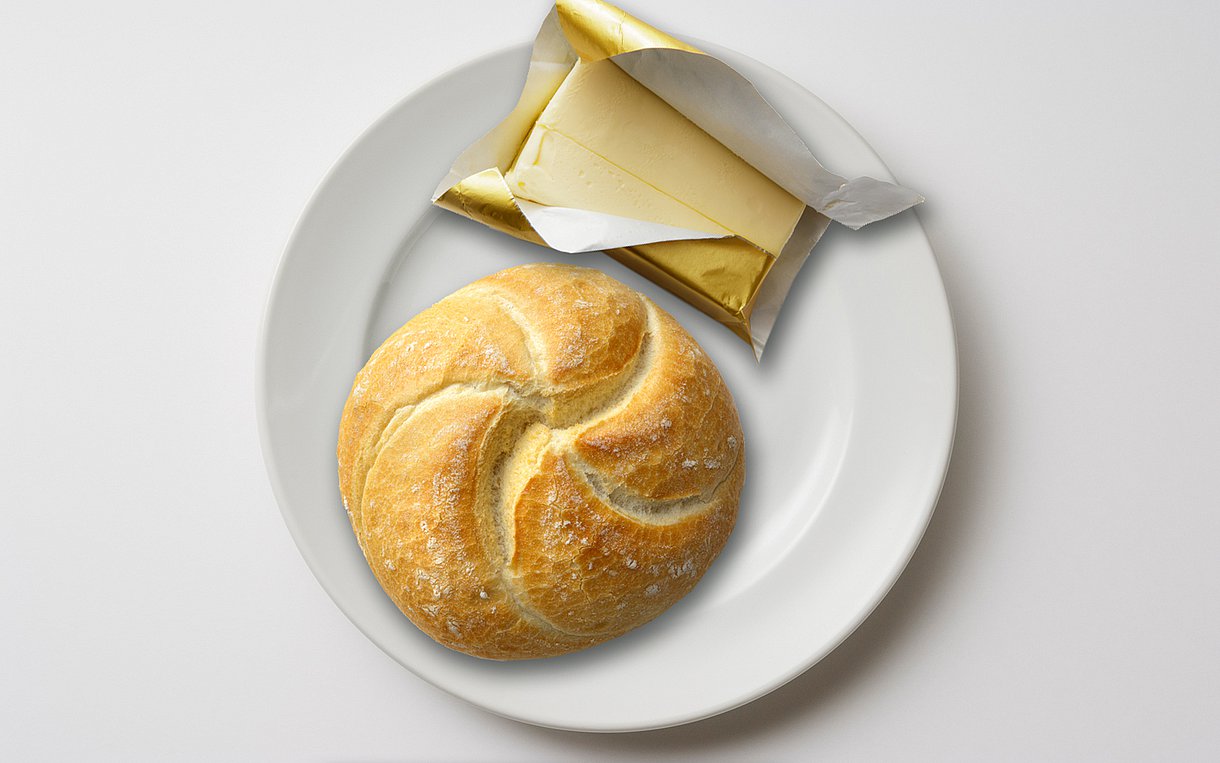 Foto eines hellen Brötchens mit einer kleinen Packung Butter daneben auf einem weißen Teller
