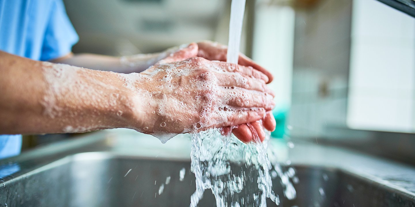 Zwei sich mit Seife waschende Hände unter dem Wasserstrahl. 