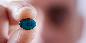 Foto: Zwei Finger halten eine PrEP-Tablette – zur Prä-Expositions-Prophylaxe von HIV.