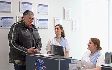Gaetano Nino Minoia an der Empfangstheke. Foto: Patient steht am Empfangstresen beim Arzt