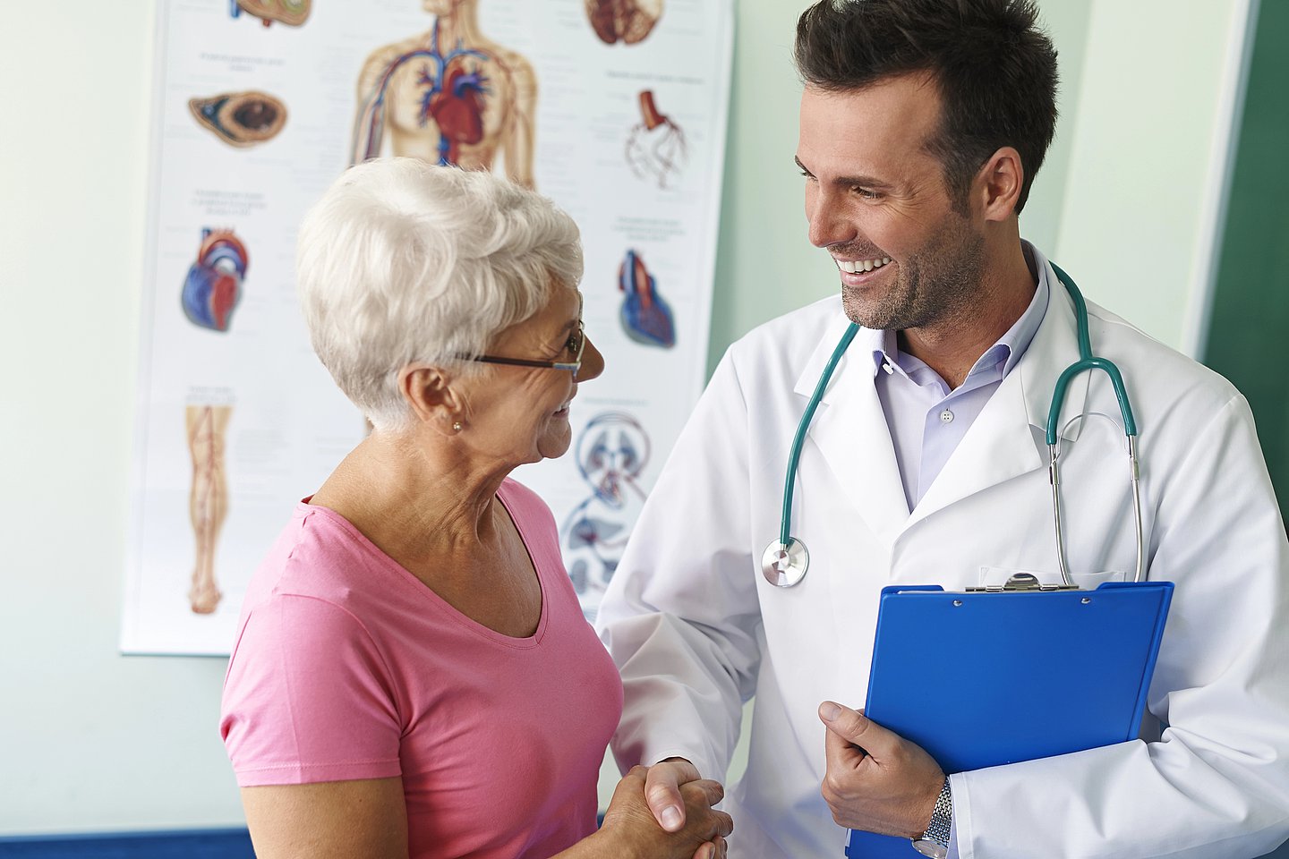 Arzt spricht mit einer älteren Patientin und gibt ihr dabei die Hand.