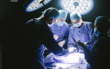 Foto eines abgedunkelten Operationssaals, in dem operiert wird