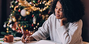 Neujahrsvorsätze Eine Frau schreibt in weihnachtlicher Atmosphäre in einem Notizbuch.