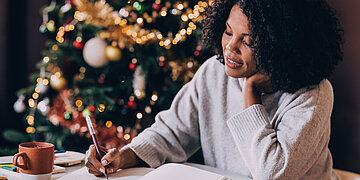 Eine Frau schreibt in weihnachtlicher Atmosph&auml;re in einem Notizbuch.