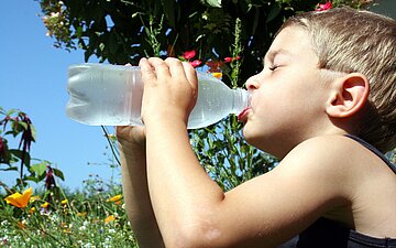 Ein Junge trinkt an einem hei&szlig;en Tag aus einer Wasserflasche.