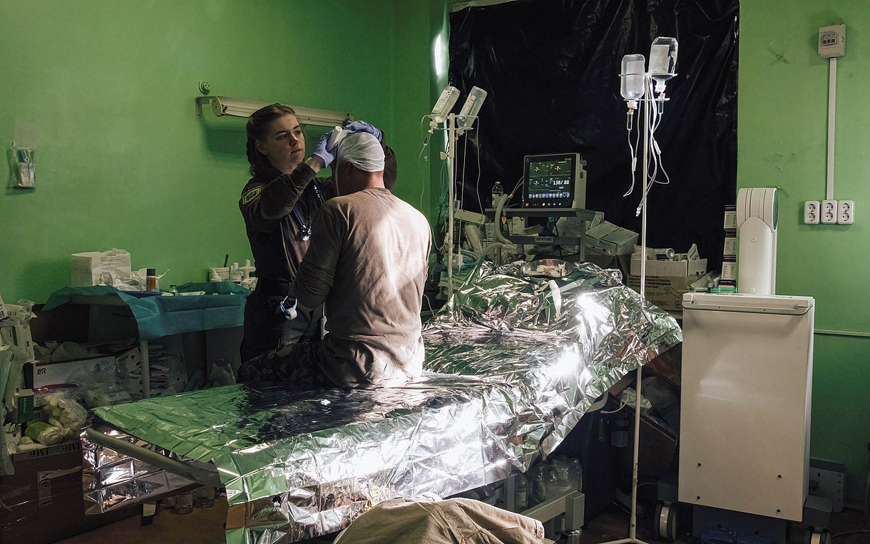 Foto einer Ärztin, die in einem Krankenzimmer einen Mann mit Kopfverletzung behandelt