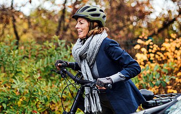 Mit dem Rad auf dem Weg zur Arbeit Das Foto einer Frau, die warm angezogen und mit Fahrradhelm, Schal und Handschuhen bekleidet ist.