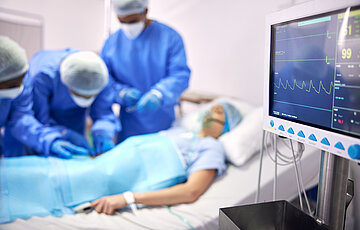 Das Foto zeigt &Auml;rzte, die eine Patientin operieren, die an einem &Uuml;berwachungsger&auml;t angeschlossen ist.