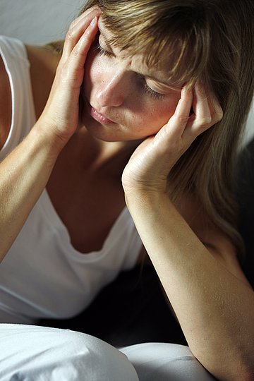Eine junge Frau hält sich den Kopf: Sie leidet unter Migräne.