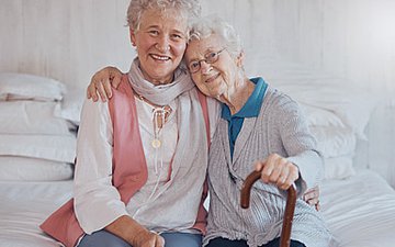 Alternative Organisationsformen ambulanter Pflege Foto: Zwei ältere Frauen sitzen auf einem Bett und umarmen sich.