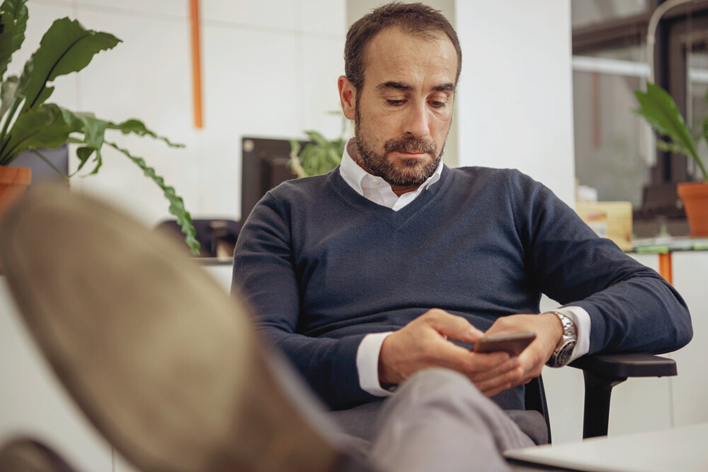 Symbolbild eines Mannes, der gemütlich auf einem Sofa sitzt und auf einem Smartphone tippt.
