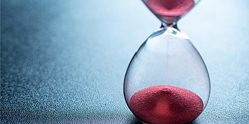 Foto: Roter Sand läuft durch eine Sanduhr.