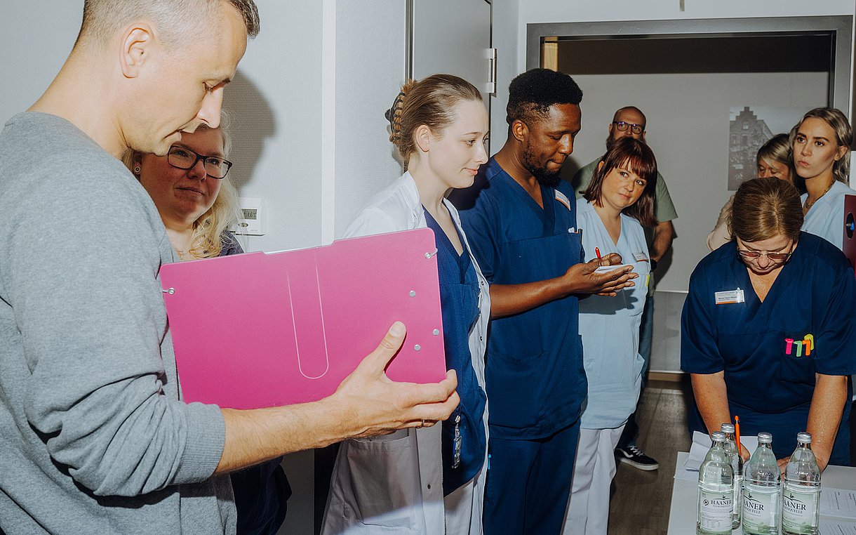 Foto des Teams des Room of Errors, die Qualitätsmanager Benedikt Körfers folgen, der eine Fallgeschichte vorliest