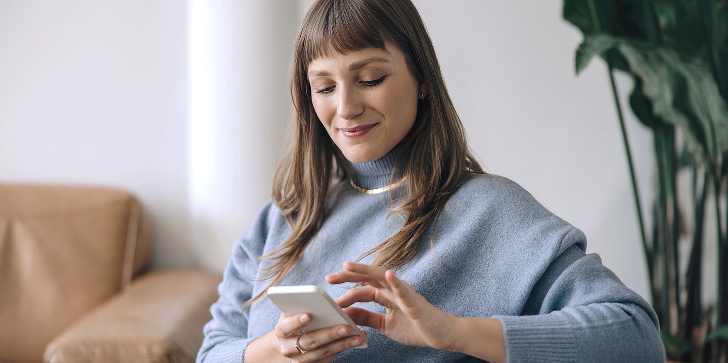 Junge Frau, die lächelnd auf ihr Handy blickt