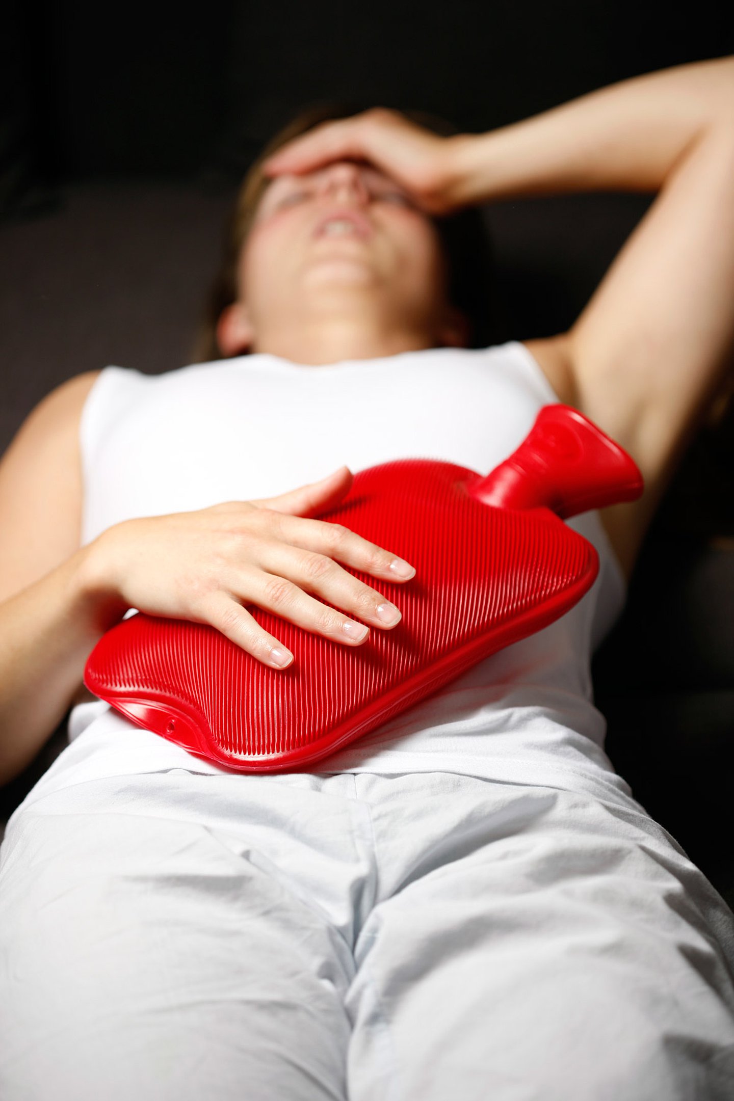 Eine junge Frau versucht mit einer Wärmflasche Schmerzen zu lindern.