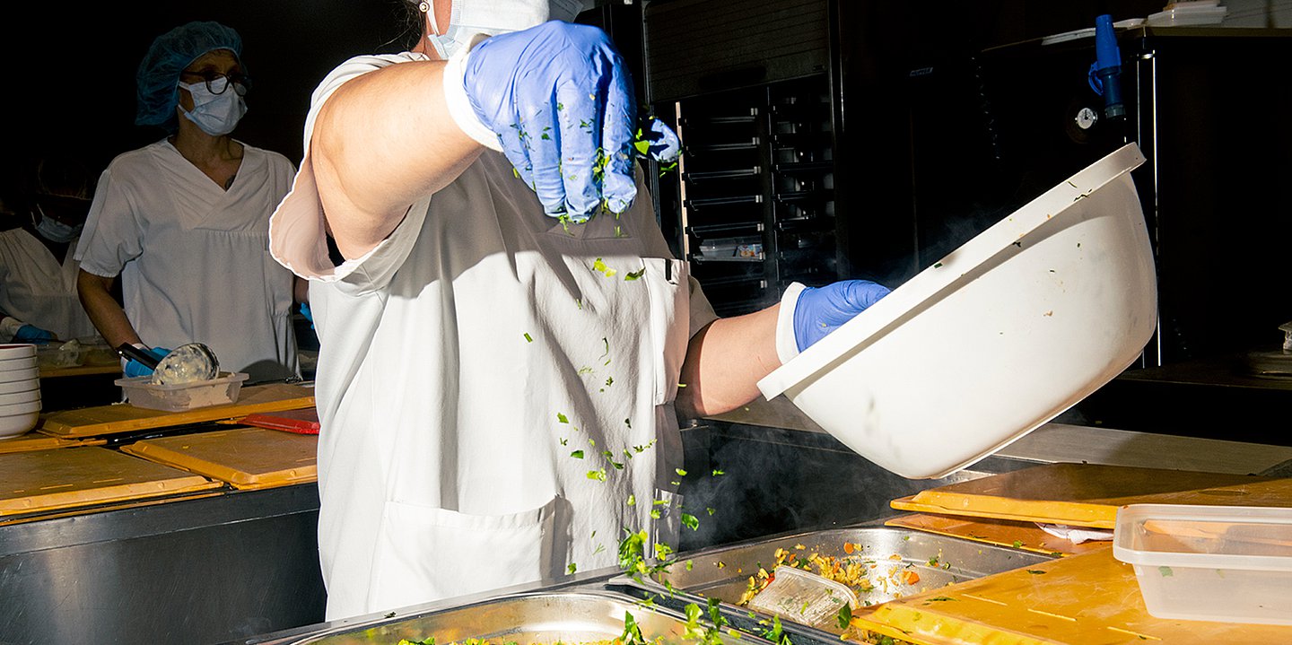 Foto eines Kochs in einer Kantine, der Gewürze über bunten Gemüsereis streut