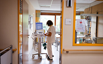 Foto: Eine Schwester in wei&szlig;er Kleidung steht an einem Computer im Schwesternzimmer der Palliativstation.
