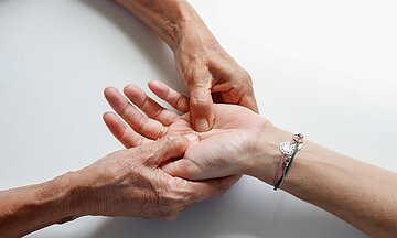Zwei H&auml;nde massieren die Innenfl&auml;che der Hand einer anderen Person.