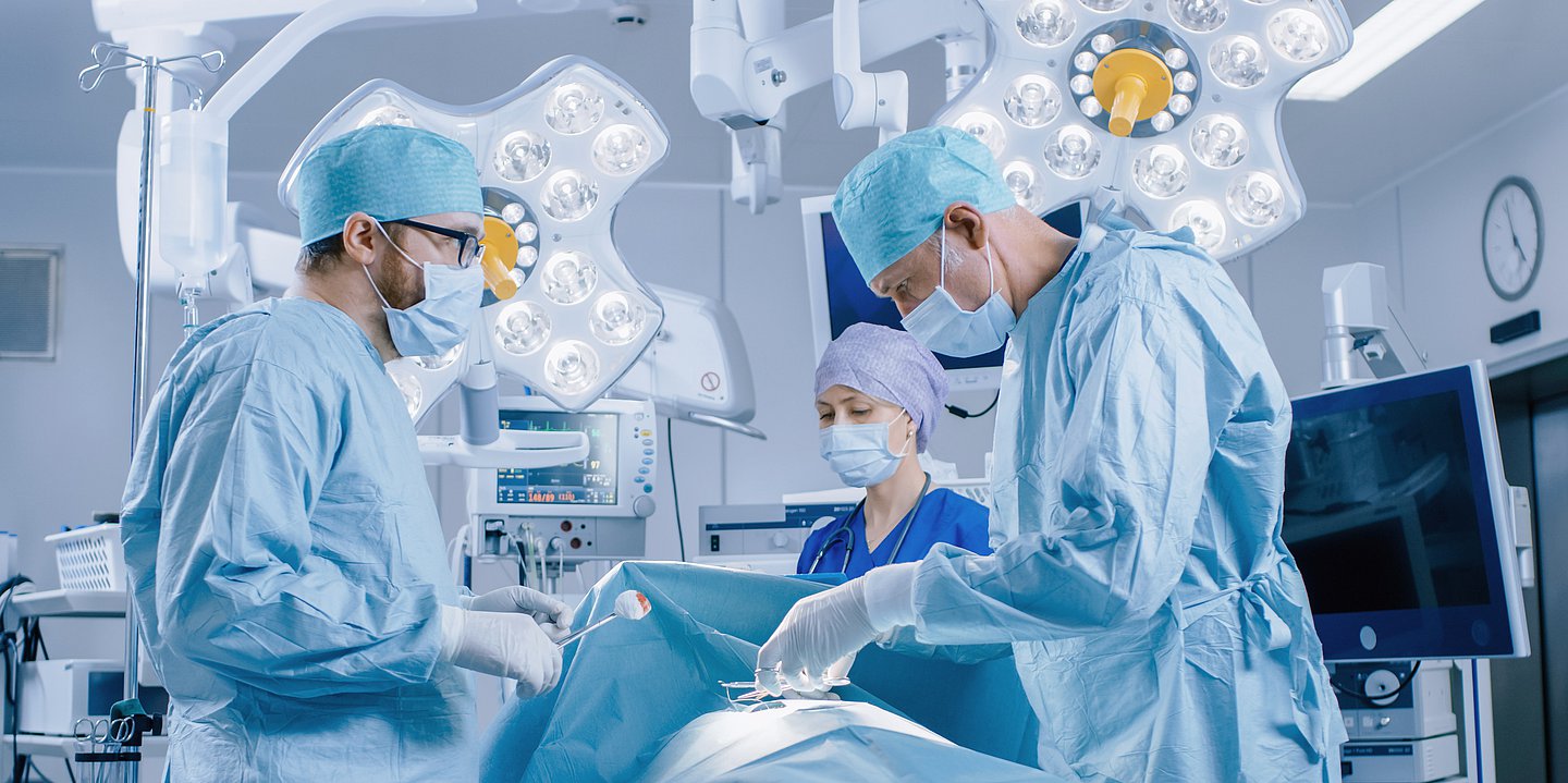 Foto: Mehrere Ärzte und Pflegekräfte sind in OP-Kleidung im OP bei einer Operation zu sehen.