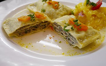 Maultaschen Ein Teller, auf dem drei geschmelzte Maultaschen liegen.