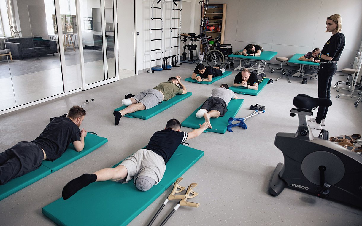 Foto zeigt ukrainische Soldaten, die im Kampf Gliedmaßen verloren haben, beim Training auf Matten in einem Rehazentrum