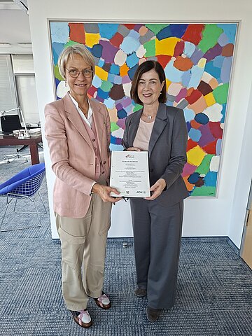 Schulministerin Dorothee Feller und AOK-Vorstandsmitglied Sabine Deutscher halten den unterzeichneten Vertrag und l&auml;cheln in die Kamera.
