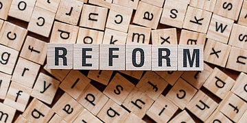 Foto: Holzbuchstaben-W&uuml;rfel liegen verteilt nebeneinander, dar&uuml;ber steht das Wort "Reform" aus Holzw&uuml;rfeln gelegt.