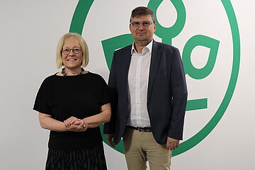 Frau Dr. Irmgard Stippler, Vorstandsvorsitzende der AOK Bayern, und Herr Dr. Wolfgang Ritter, Landesvorsitzender des BH&Auml;V, stehen gemeinsam vor einem Transparent mit dem AOK-Logo mit dem Lebensbaum