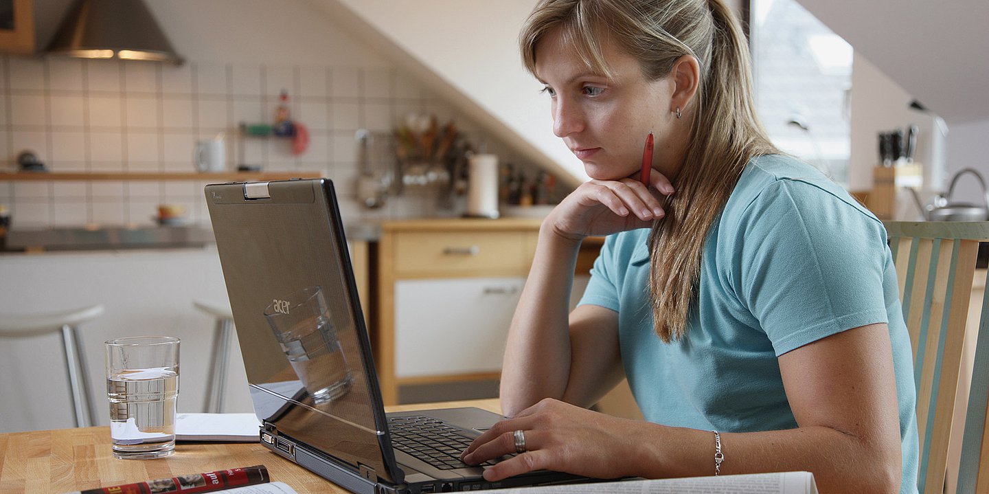 Foto zeigt eine Frau, die vor einem Laptop sitzt und liest.