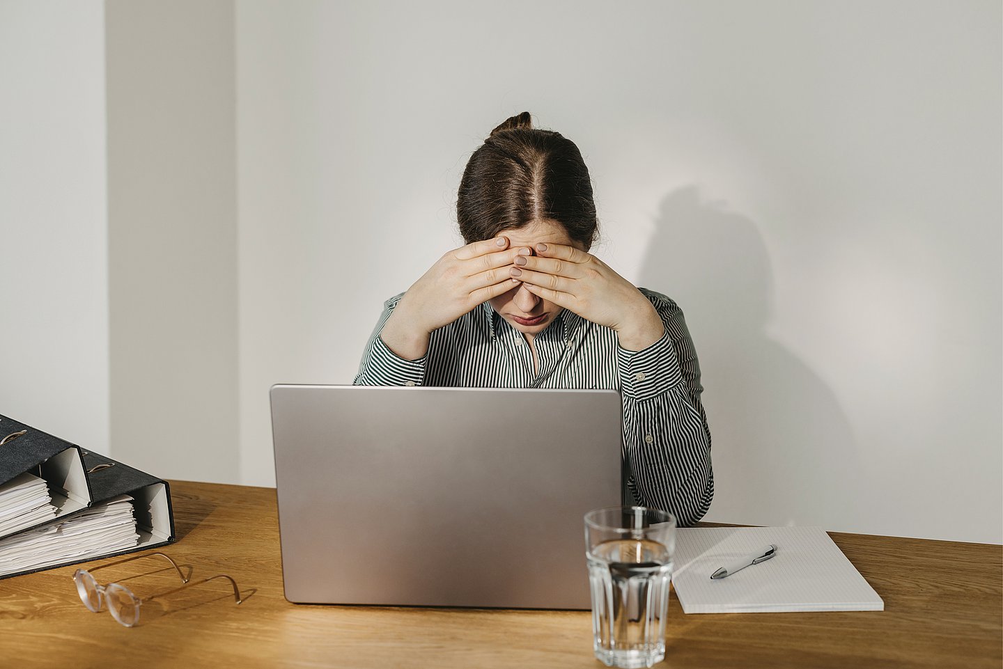 Eine Frau sitzt an einem Notebook, um zu arbeiten. Ihre Körpersprache zeigt, dass sie sich unwohl fühlt und wahrscheinlich krank wird.