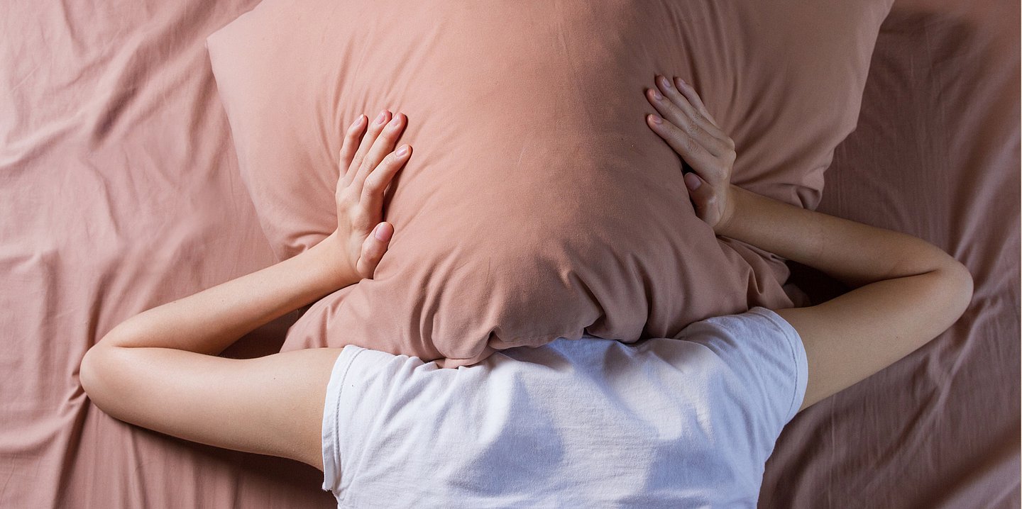 Foto einer Person, die sich ein Kissen über den Kopf drückt